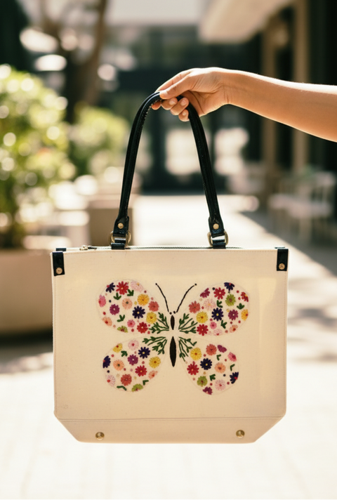Hand holding a tote bag with a floral butterfly design outdoors.